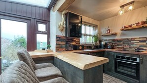 A modern kitchen with a built-in island, seating area, and a large window. - 1 bedroom accommodation in Abergele (Abergele)
