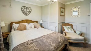A bedroom with a large bed, a chair, a heart-shaped wall decoration, and a chandelier. - 1 bedroom accommodation in Abergele (Abergele)