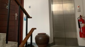 Una escalera con barandillas de madera, un jarrón de cerámica grande, un ascensor y un extintor en la pared.