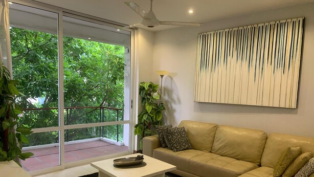 Una sala de estar moderna con un sofá color beige, una mesa de centro blanca y un ventanal con vistas a zonas verdes.