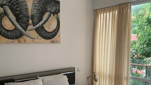 Un dormitorio con una cama, ventilador de techo, ventana con cortinas y un cuadro en la pared.