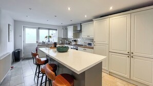 A modern kitchen with a central island, bar stools, and white cabinetry. - 4 bedroom accommodation in Beaumaris (Beaumaris)
