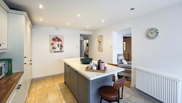 A modern kitchen with a central island, a dining area with a chair, and a clock on the wall. - 4 bedroom accommodation in Beaumaris (Beaumaris)