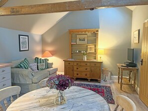 A cozy room with a wooden ceiling, a sofa, a table with a vase of flowers, a dresser, a mirror, and a television on a wooden stand. - Coach House Cottage - UK50964 (Kirklington, near Bedale)
