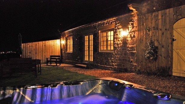 Un bâtiment en pierre avec un jacuzzi à l’avant, une clôture en bois et un banc.
