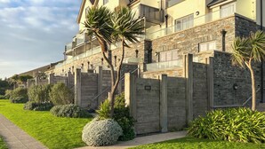 Un edificio residencial de varios pisos con fachada de piedra, un balcón y un césped bien cuidado.