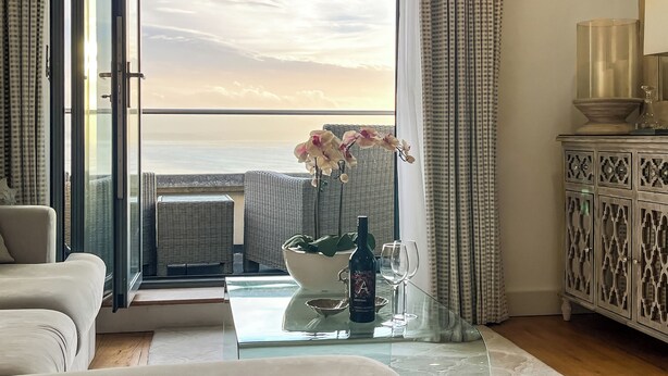 Una habitación con una mesa de vidrio, una botella, dos vasos, un sofá y vistas al mar.