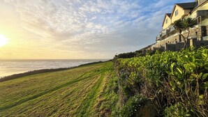 Una propiedad costera con zona verde, pared de piedra y edificio con balcones con vista al mar.