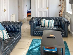 Ein Wohnzimmer mit zwei dunkelbraunen Ledersofas, einem passenden Couchtisch und einem blauen Teppich.