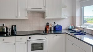 Eine Küche mit weißen Schränken, einer schwarzen Arbeitsplatte, einem eingebauten Backofen und einem Fenster mit Blick ins Grüne.