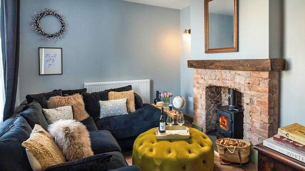 A cozy living room with a dark blue sofa, a yellow ottoman, a fireplace, and a mirror on the wall. - 3 bedroom accommodation in Llandundo Junction (Llandundo Junction)