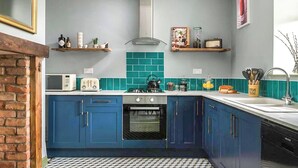 A kitchen with blue cabinets, a gas stove, a microwave, and a tiled backsplash. - 3 bedroom accommodation in Llandundo Junction (Llandundo Junction)