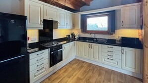Eine moderne Küche mit weißen Schränken, einem schwarzen Kühlschrank und einer Holzbalkendecke.