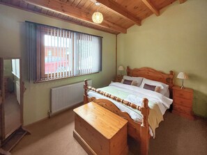 A bedroom with a wooden bed, a nightstand, a dresser, a window with blinds, and a radiator. - A wonderful lakeside escape for all ages. (Horncastle)