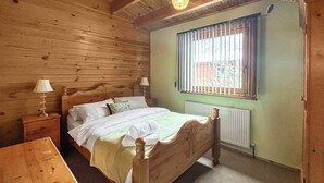 Ein Schlafzimmer mit Holzwandverkleidung, ausgestattet mit einem Einzelbett, einem Nachttisch, einem Tisch und einem Fenster mit Jalousien.