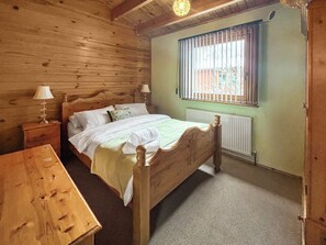 Ein Schlafzimmer mit Holzwandverkleidung, ausgestattet mit einem Einzelbett, einem Nachttisch, einem Tisch und einem Fenster mit Jalousien.