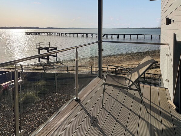 Une terrasse en bois avec une rambarde donnant sur une plage et une jetée.