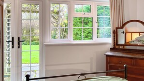 A bedroom with a bed, a wooden dresser, a mirror, and a window with a view of a garden. - 3 bedroom accommodation in Ibberton, near Blandford Forum (Ibberton, near Blandford Forum)