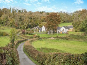 A rural setting with a pathway leading to a cluster of stone houses surrounded by greenery and trees. - Carreg Gwenlais Barn (Llandybie Ammanford, near Llandeilo)