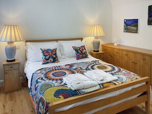 A neatly made bed with colorful pillows, a bedside lamp, and a wooden nightstand. - Carreg Gwenlais Barn (Llandybie Ammanford, near Llandeilo)