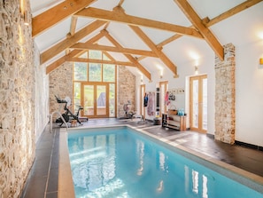 An indoor swimming pool with stone walls and wooden beams, exercise equipment, and a view of greenery outside. - Carreg Gwenlais Barn (Llandybie Ammanford, near Llandeilo)