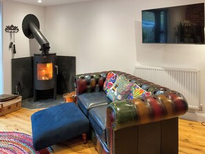 Een woonkamer met een bank, een open haard, een televisie en een radiator.