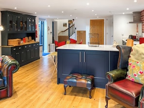 A modern kitchen with dark cabinetry, a central island, and a staircase leading to an upper level. - Carreg Gwenlais Barn (Llandybie Ammanford, near Llandeilo)