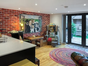 A modern living room with a brick wall, a dining area, a colorful rug, and a large window.