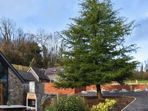 A stone building with a tiled fireplace, a brick wall, and a large evergreen tree.