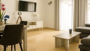 Ein modernes Wohnzimmer mit Flachbildfernseher, Schreibtisch mit Lampe, Sessel, Sofa und Couchtisch.
