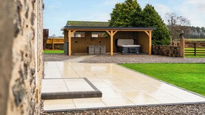A covered outdoor area with a barbecue grill, seating, and a stone wall.