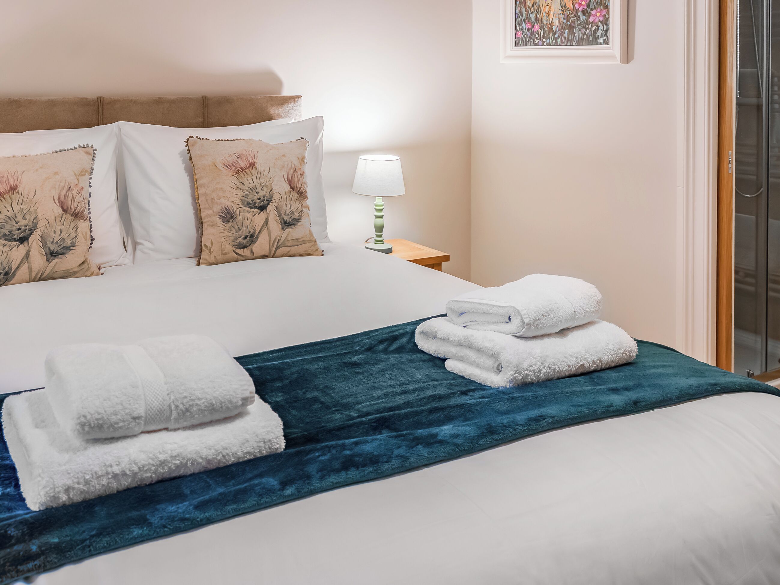 Ein ordentlich bezogenes Bett mit weißen Laken, einer blauen Tagesdecke und zwei gefalteten Handtüchern.