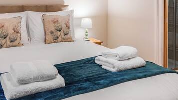 Ein ordentlich bezogenes Bett mit weißen Laken, einer blauen Tagesdecke und zwei gefalteten Handtüchern.