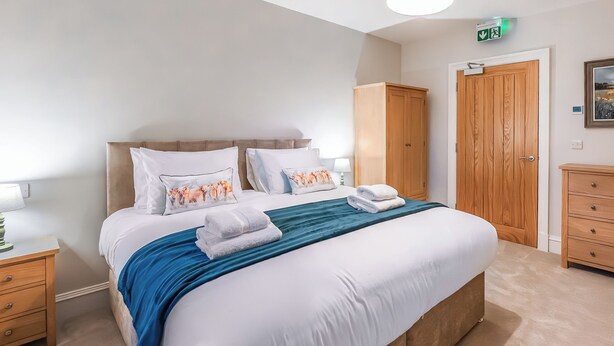 A neatly made bed with white linens and a blue throw, a wooden wardrobe, and a wooden cabinet with drawers.