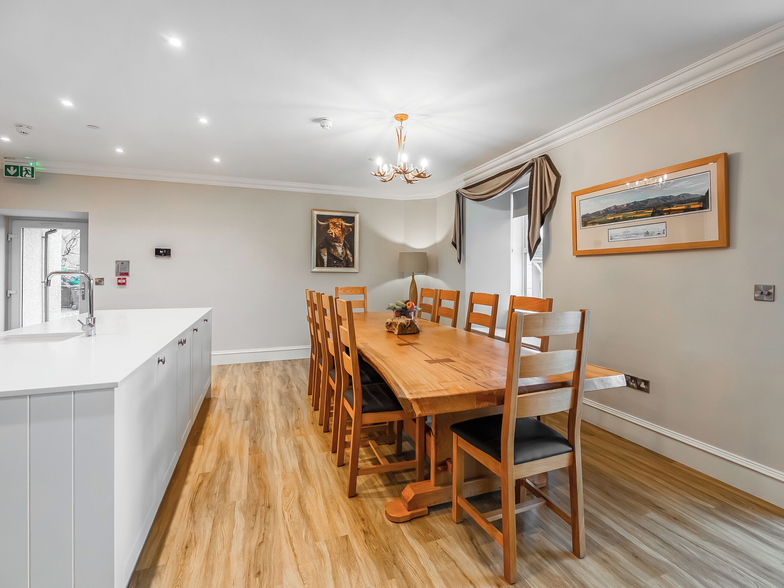 A dining area with a wooden table and chairs, a chandelier, and a framed picture on the wall.