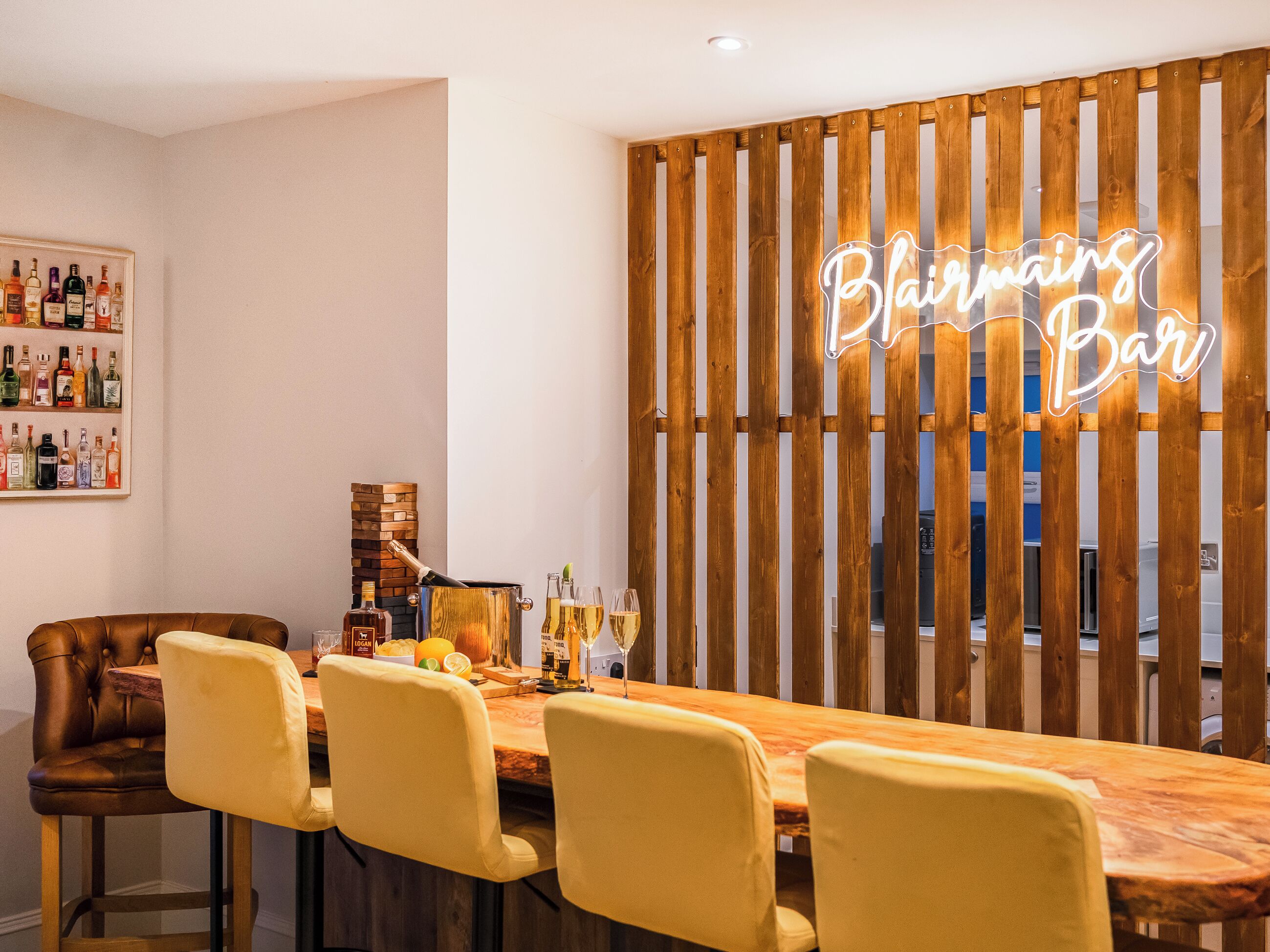 A dining area with a wooden partition, a neon sign reading 'Blairmin's Bar,' and a bar counter with bottles and glasses.