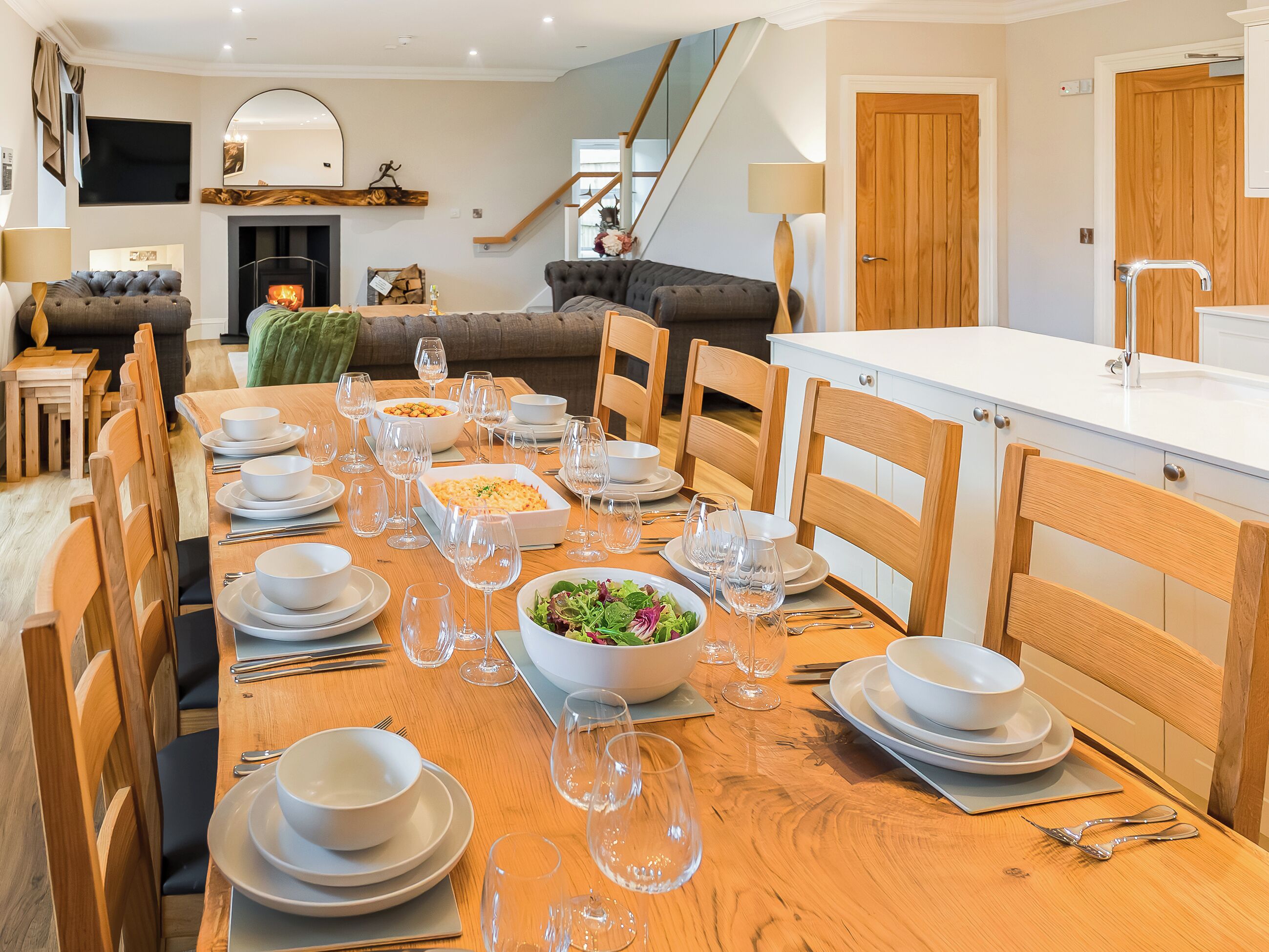 A dining area with a long wooden table set for a meal, surrounded by wooden chairs.