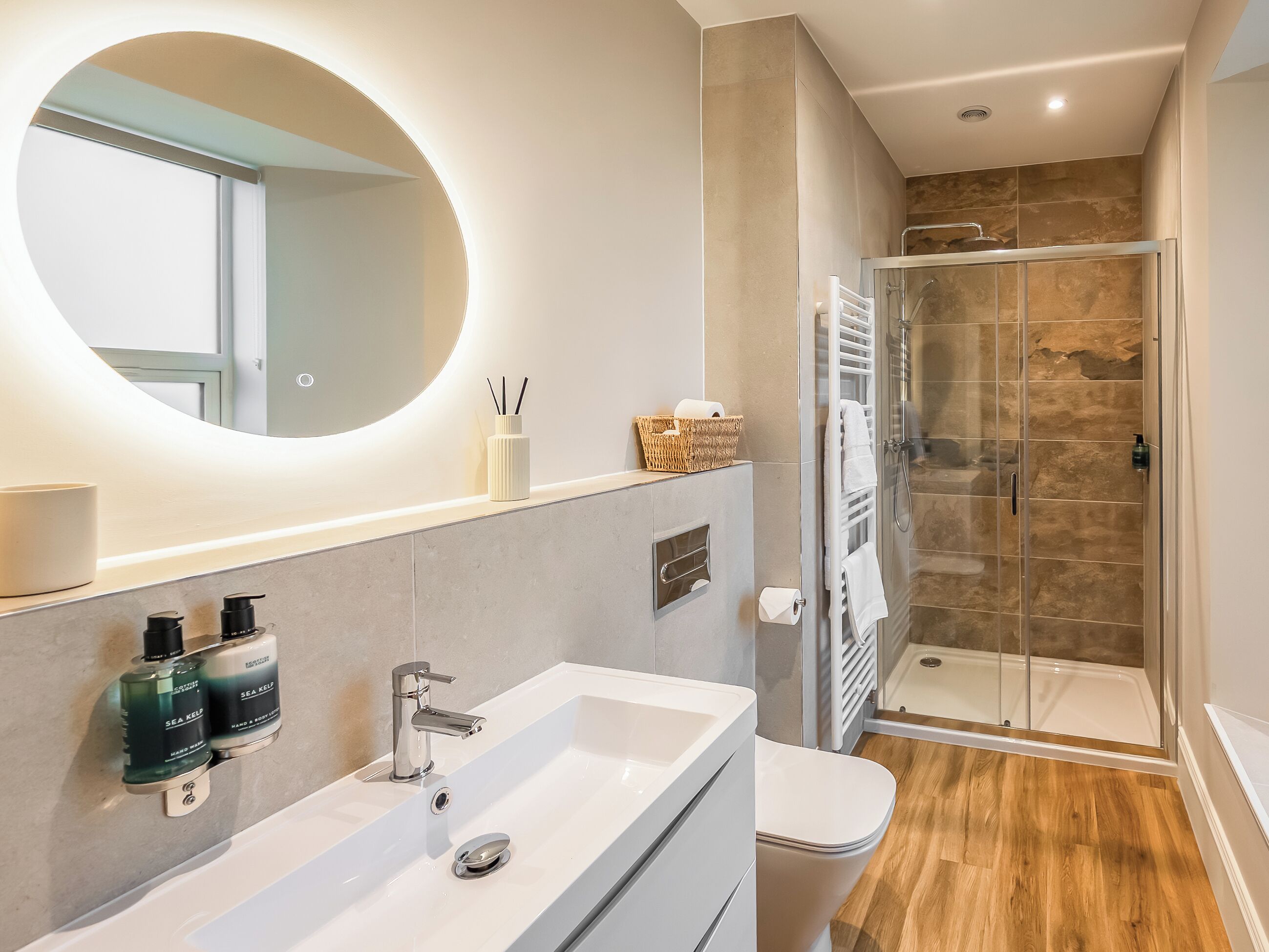 A modern bathroom with a large mirror, a white sink, and a glass-enclosed shower.