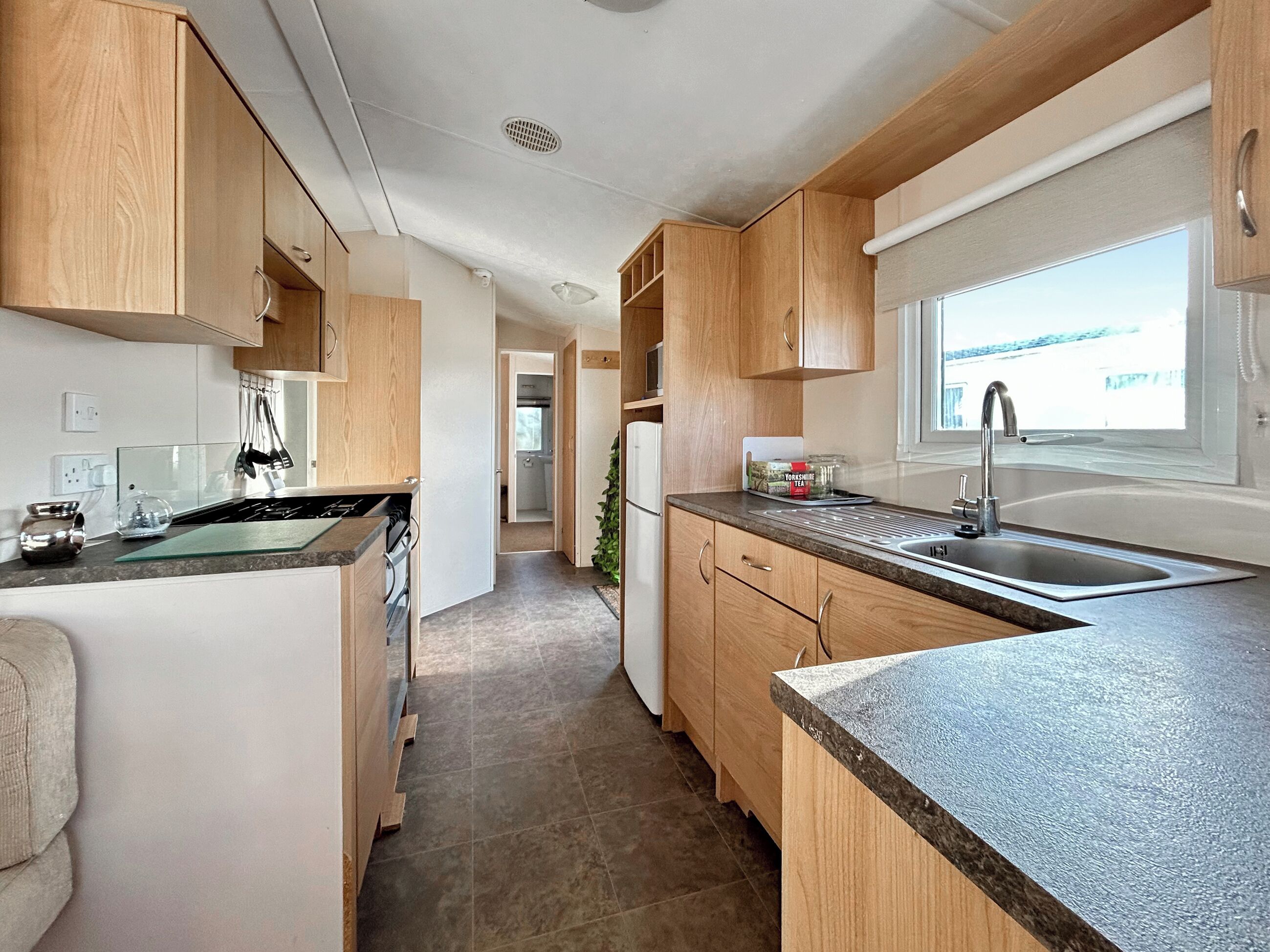 Una cocina moderna con armarios de madera, un lavamanos de acero inoxidable y un ventanal que proporciona luz natural.