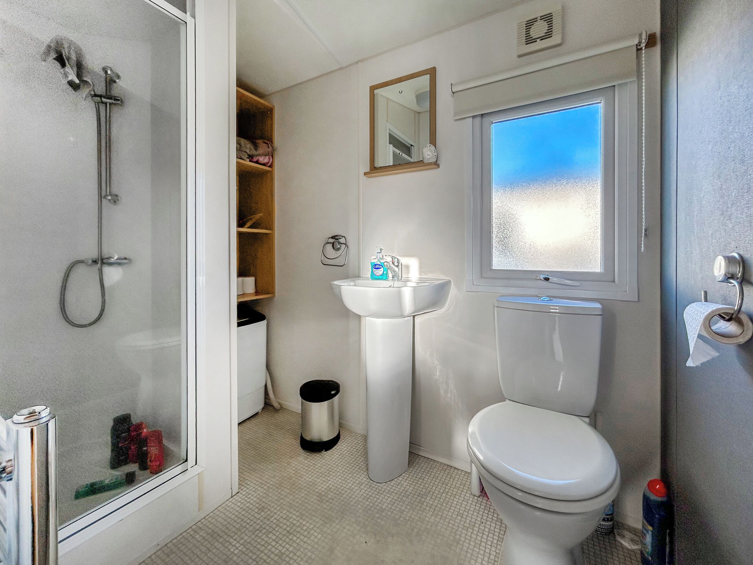 A bathroom with a shower, sink, toilet, and a window with a view.