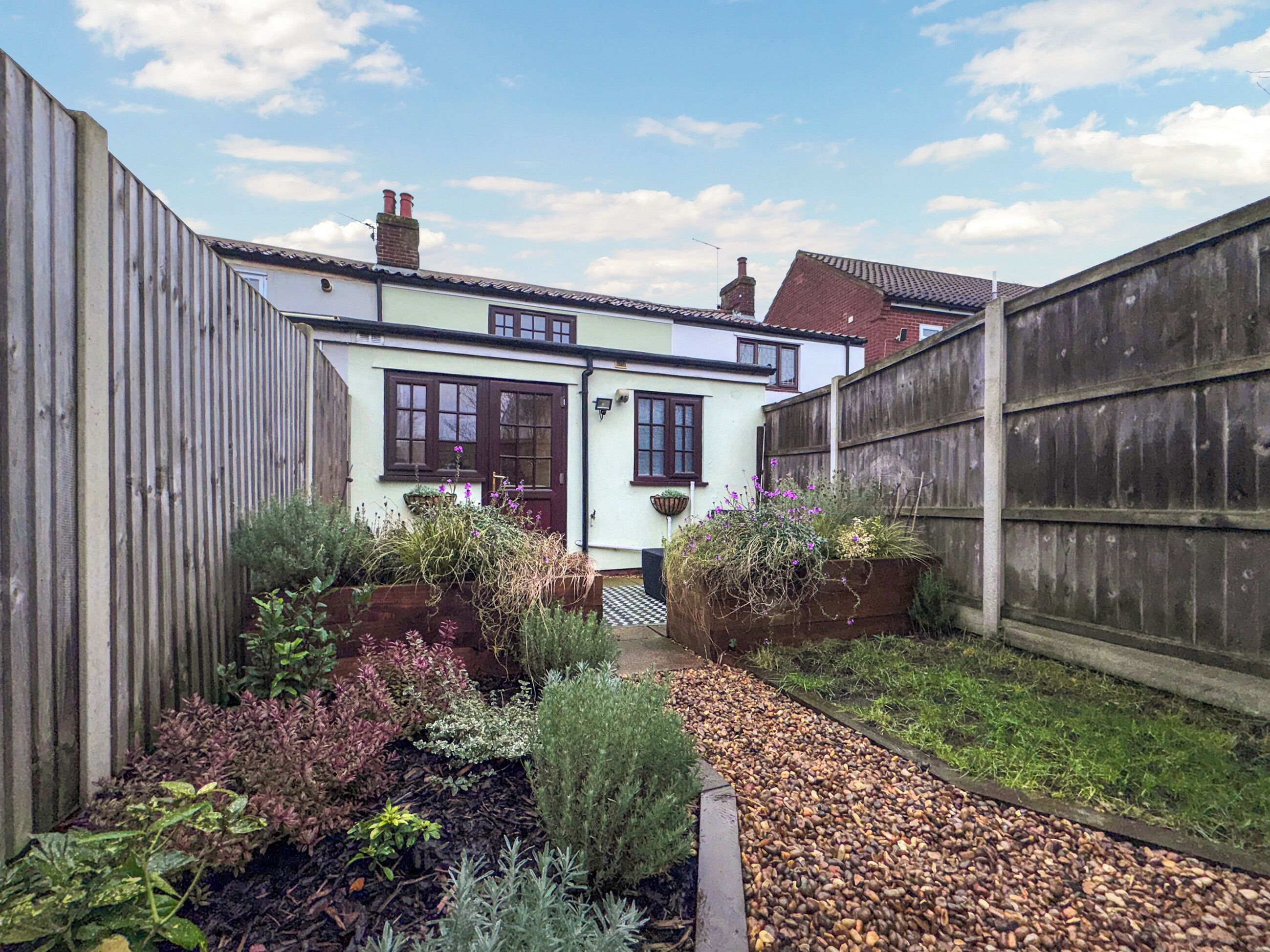 A narrow garden path leading to a house with a white facade and dark brown windows.