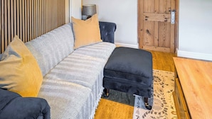 Ein gemütliches Wohnzimmer mit einer Couch, einem Hocker und einer Holztür.