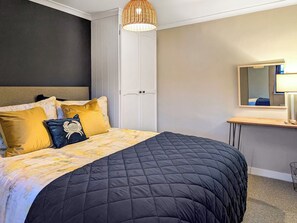 Un dormitorio ordenado con una cama grande, una mesita de noche, un espejo y una lámpara colgante.
