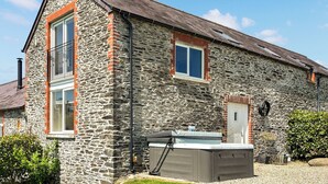 A stone building with a sloped roof, a chimney, and a small attached structure with a hot tub. - 3 bedroom accommodation in Boncath (Boncath)