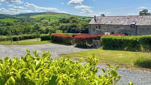 A stone building with a gravel driveway and a lush green landscape in the background. - 3 bedroom accommodation in Boncath (Boncath)