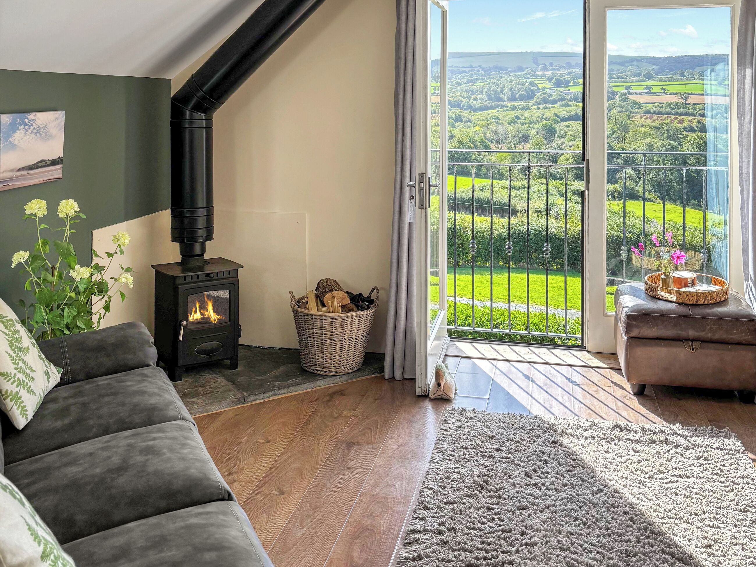Ein gemütliches Wohnzimmer mit Kamin, einer Couch und Blick auf eine grüne Landschaft durch eine Glastür.