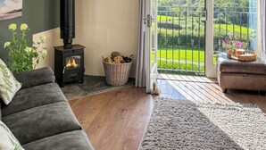 A cozy living room with a fireplace, a sofa, and a view of a green landscape through a glass door. - 3 bedroom accommodation in Boncath (Boncath)