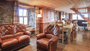 Ein gemütliches Zimmer mit Ledersofa und Sessel, einer Holztreppe und einer Steinwand.