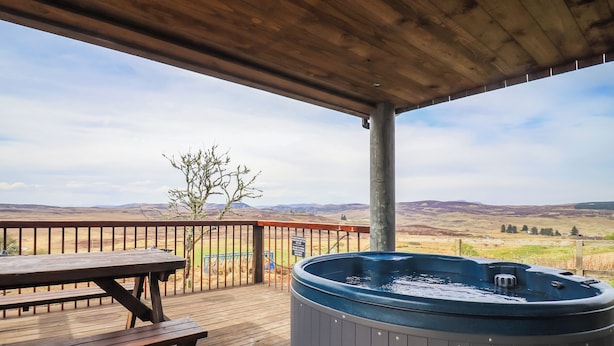 Eine Holzterrasse mit Whirlpool, Picknicktisch und Blick auf sanfte Hügel.