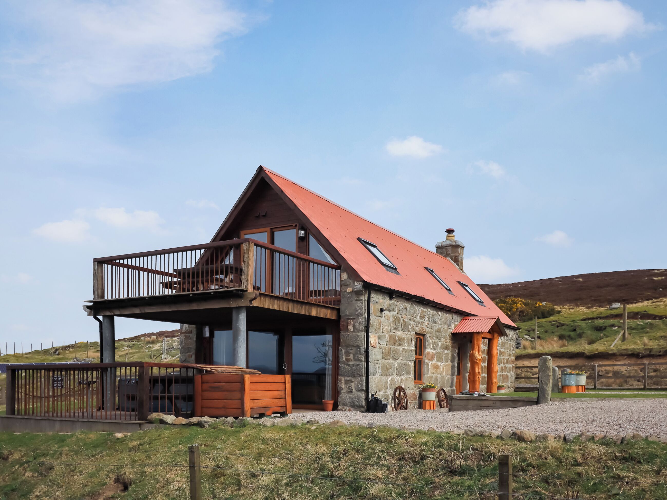 A stone house with a red roof, a balcony, and a chimney.